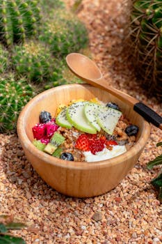 Fresh fruit bowl with yogurt and granola surrounded by cacti. Perfect healthy breakfast in a rustic setting.