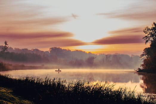 A tranquil sunset scene featuring a lone boat on a misty lake with vivid reflections and vibrant colors.