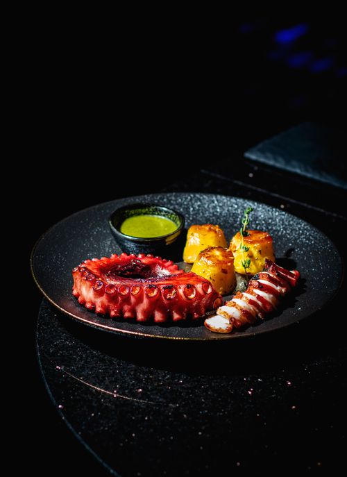 Free Delicious octopus served with sauce and vegetables on elegant black plate. Stock Photo