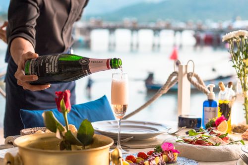 Free A waiter pours champagne at an elegant outdoor dining setup by the sea, creating a luxurious atmosphere. Stock Photo