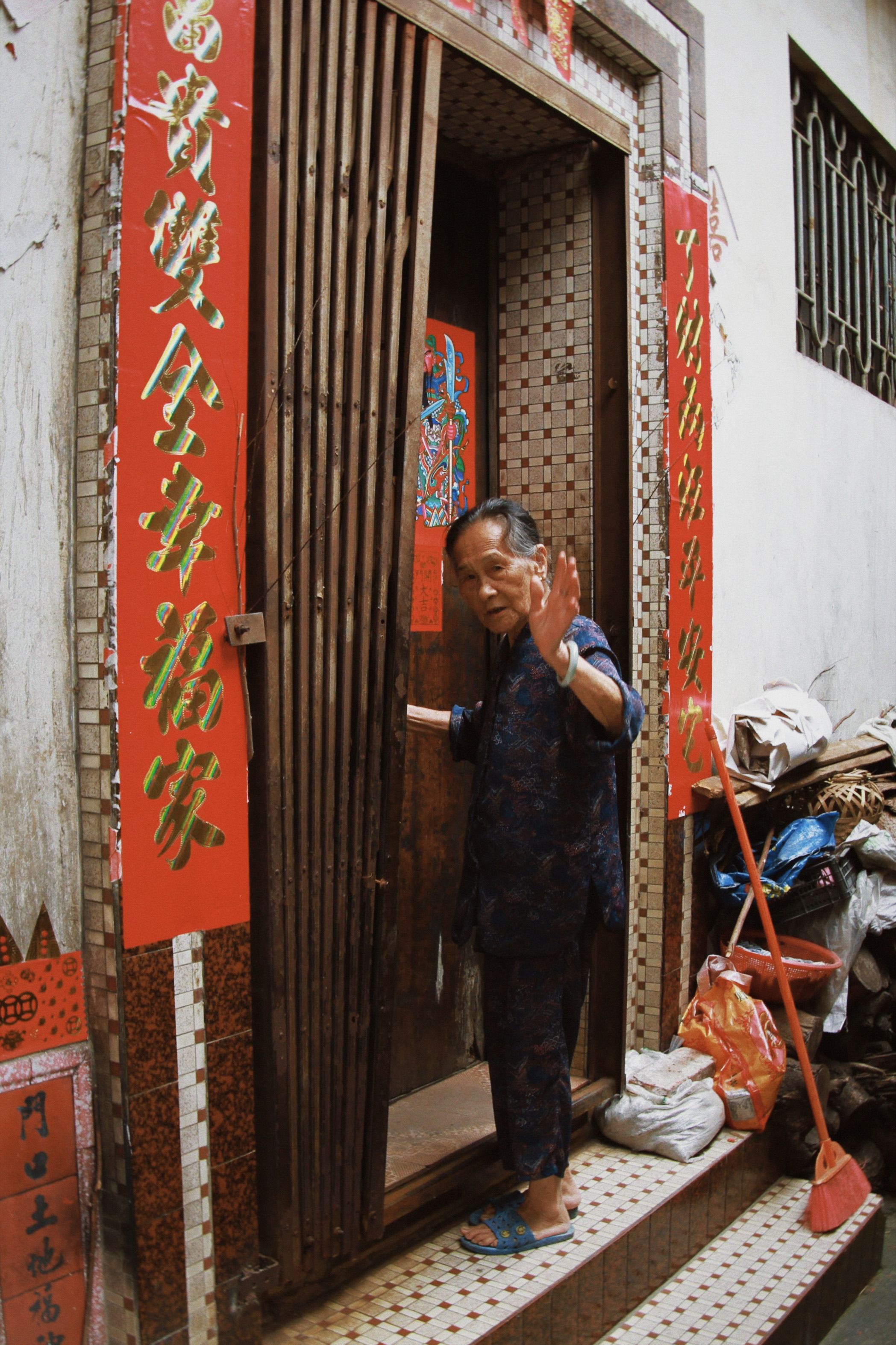 An elderly individual gesturing at a traditional entrance adorned with Chinese decorations.