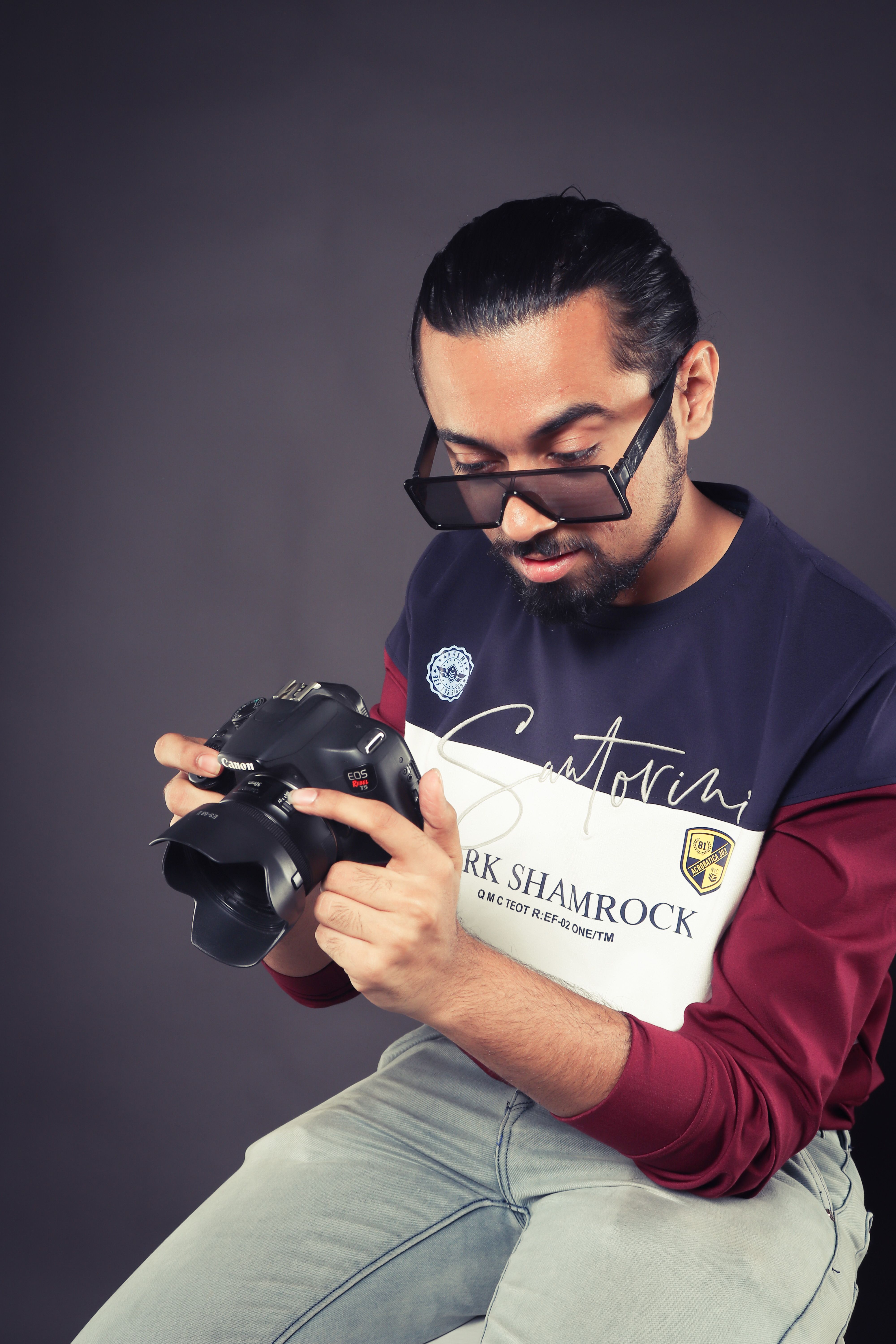 A photographer wearing sunglasses examines a camera in a studio shoot.