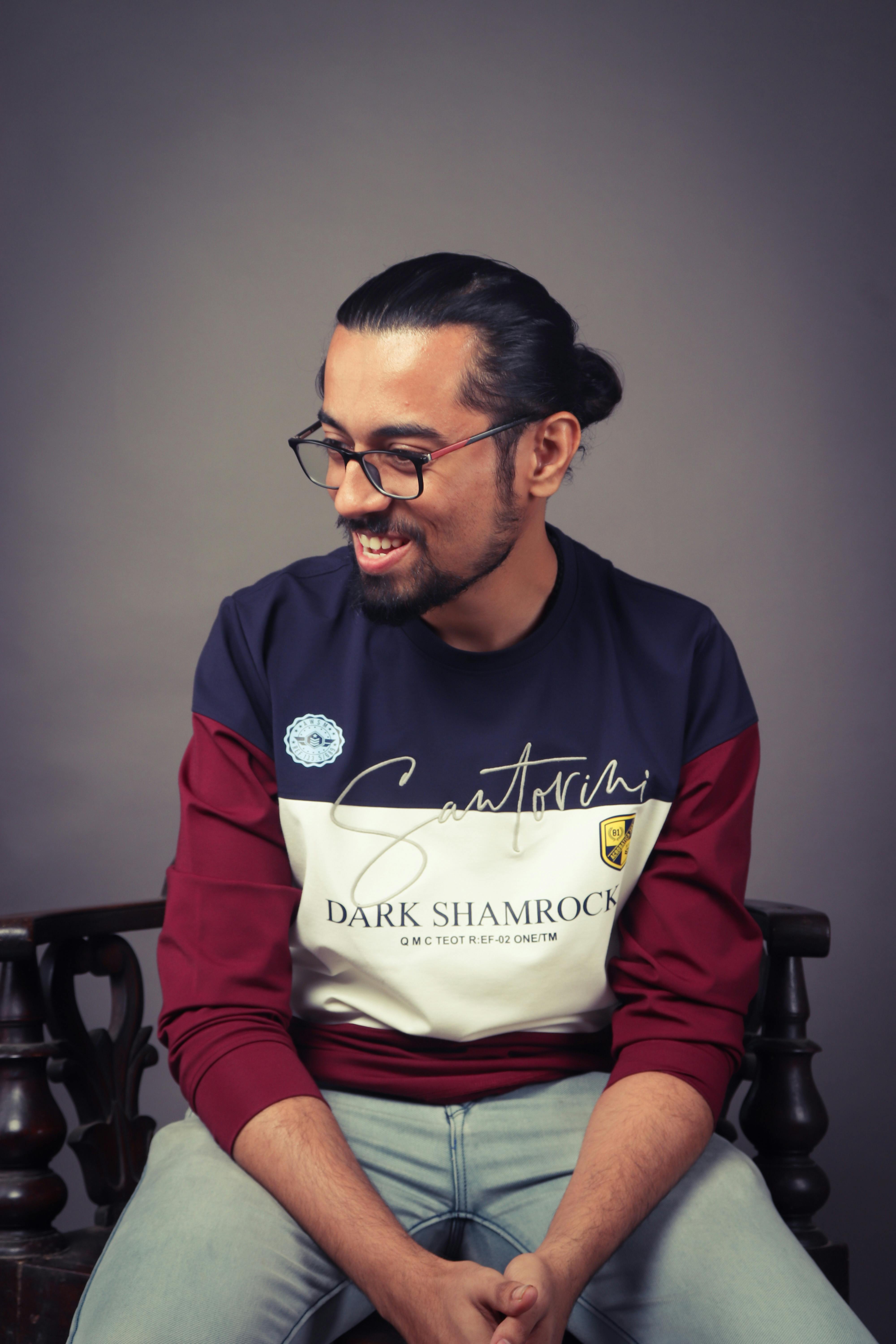 Studio portrait of a casually dressed man with glasses and a smile, wearing a Santorini-themed sweatshirt.