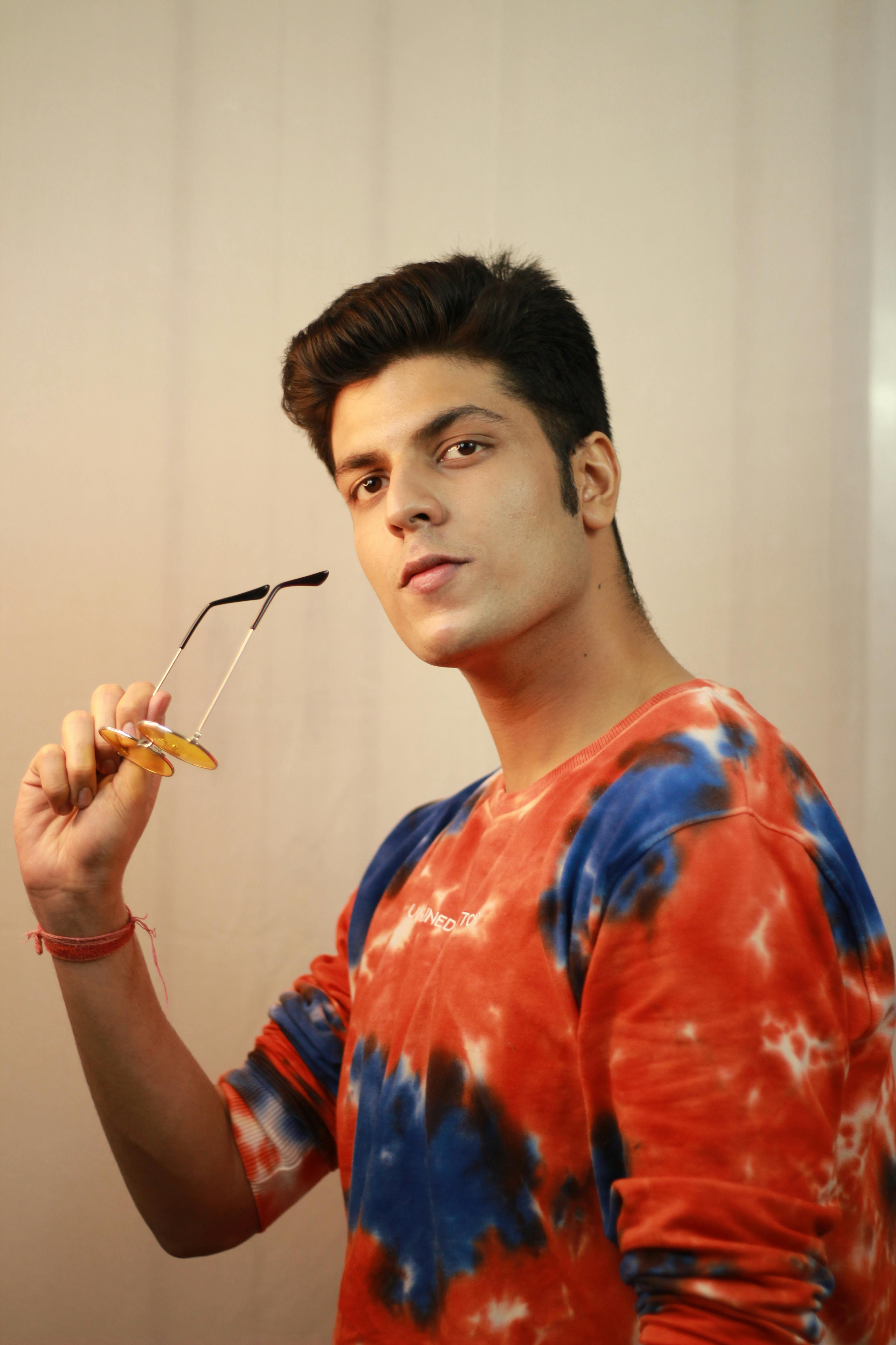 Stylish young man in a colorful tie-dye shirt holding sunglasses, showcasing modern fashion.
