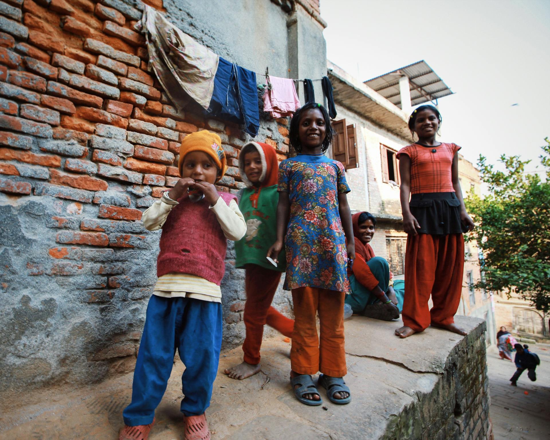 Group of smiling children playing next to a rustic brick wall in an urban setting.