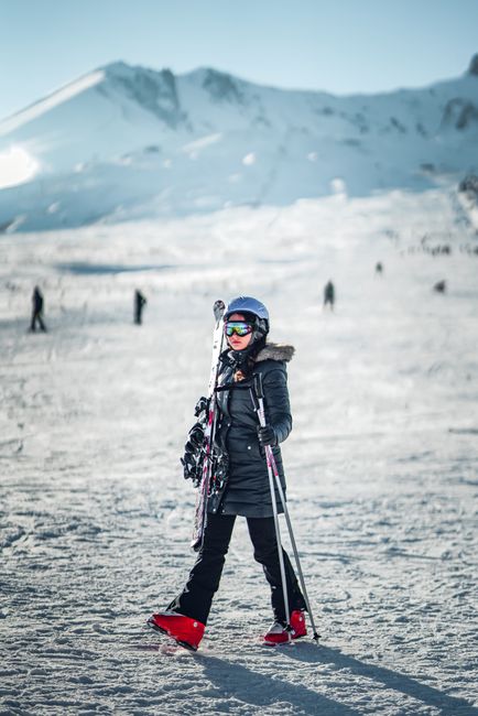 An adult skier in winter gear on a snowy mountainside, holding skis and enjoying the outdoors.