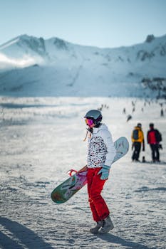 A woman snowboarder in colorful gear stands on a snowy mountain slope, enjoying a winter day.
