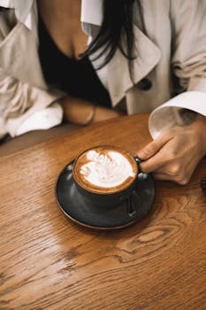 A stylish woman holds a beautifully crafted latte in a cozy coffee shop setting.