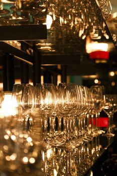 A close-up view of neatly arranged wine glasses in a dimly lit bar, reflecting warm light.