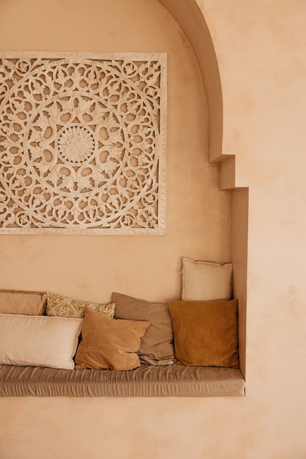 Cozy indoor seating with decorative pillows and intricate wall decor in warm beige tones.