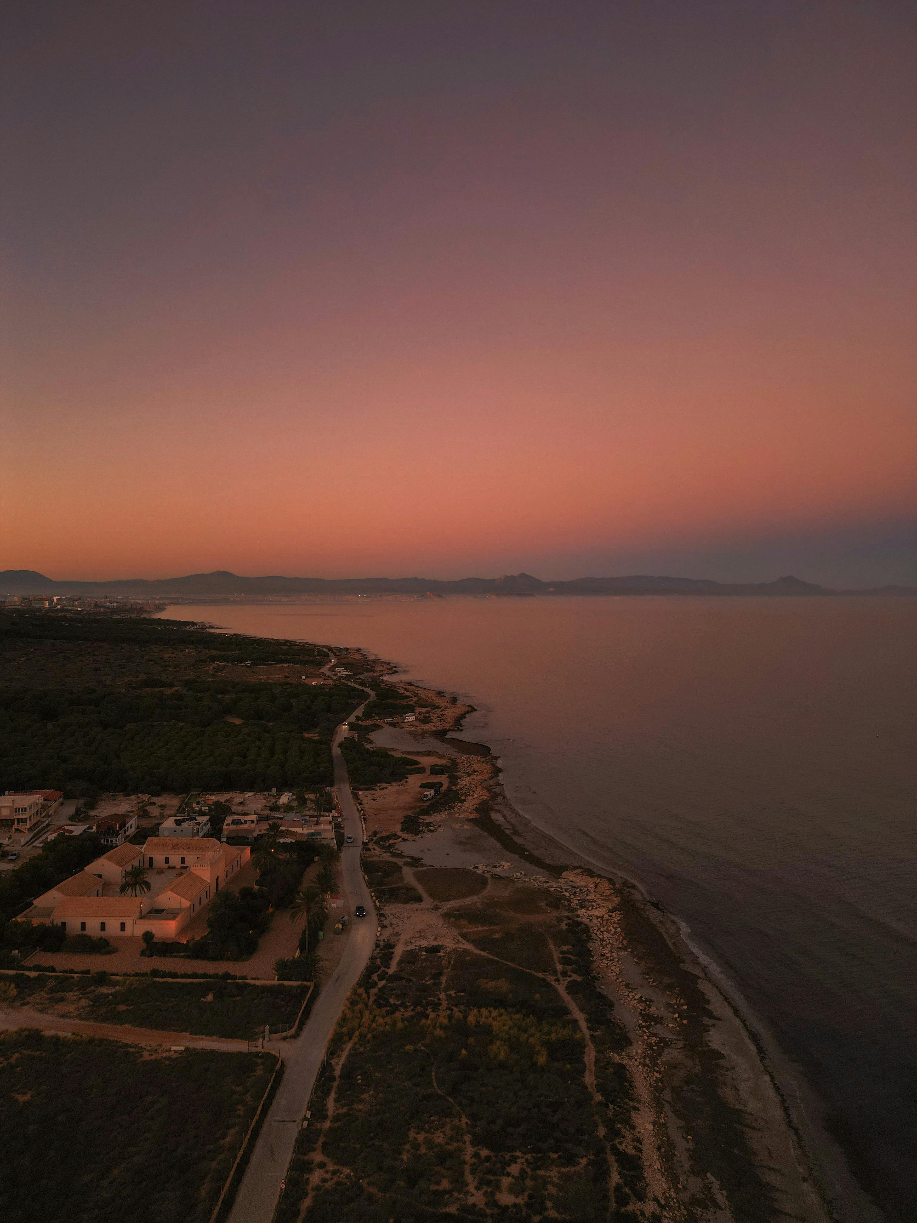 Serene aerial shot of Gran Alacant coastline at sunset, capturing the warm hues of the sky and tranquil sea.