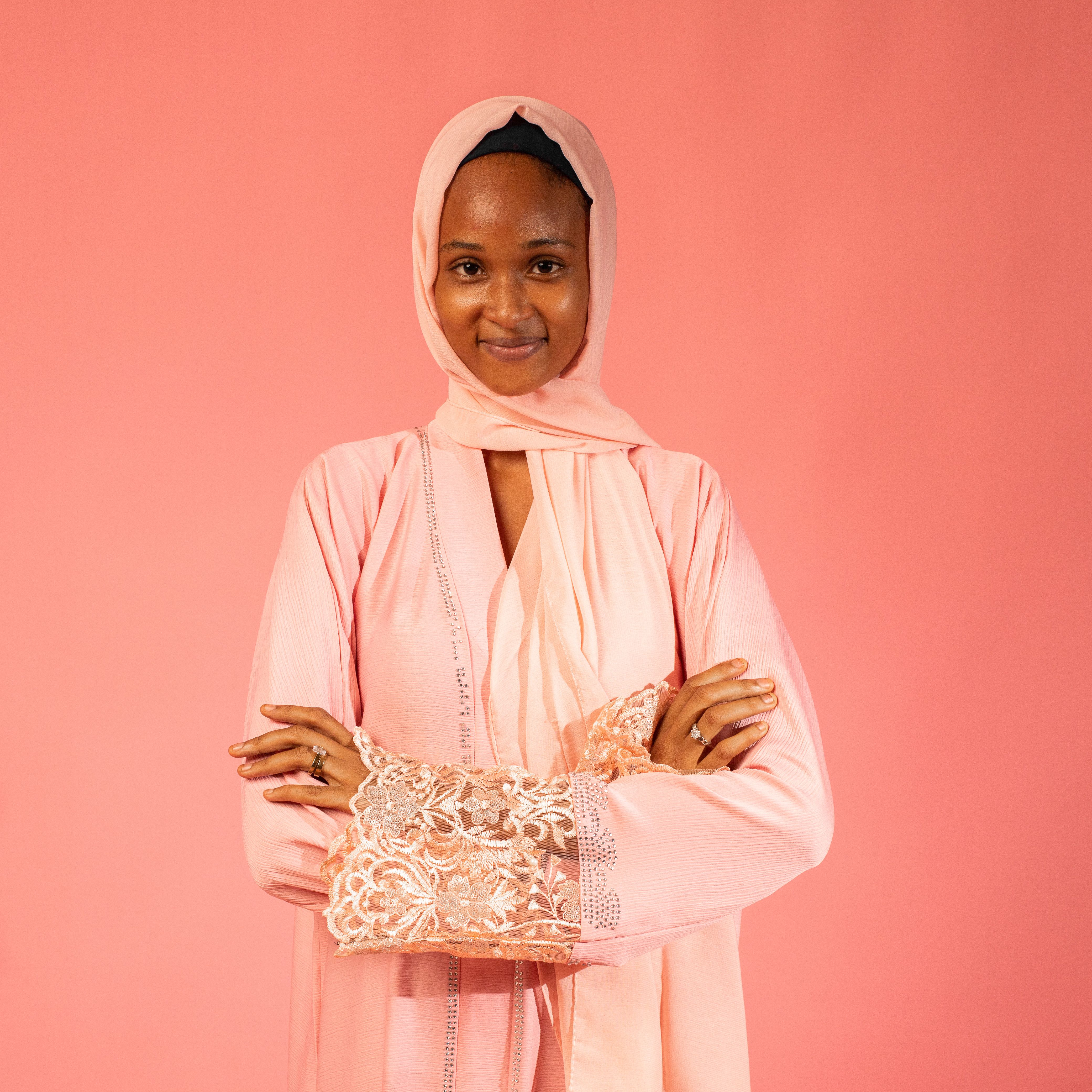 Portrait of a smiling African woman in a pink headscarf and robe against a matching background.