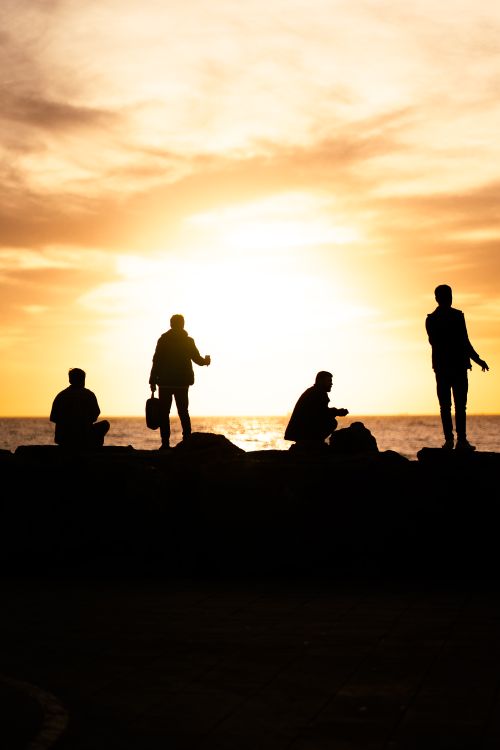 Free Silhouettes of people on the shore during a vibrant sunset over the ocean. Stock Photo