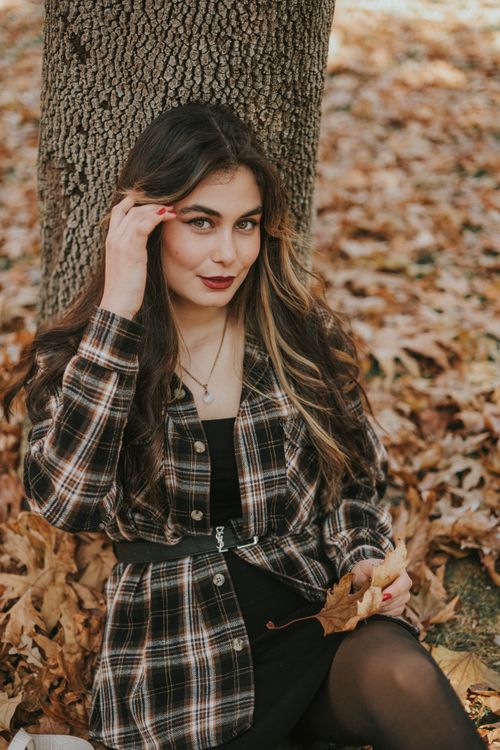 Free Charming young woman in checkered attire posing in a park surrounded by autumn leaves. Stock Photo