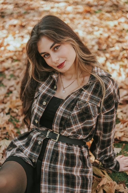 Free Vibrant autumn portrait of a woman with long brown hair, sitting amidst fall leaves in a plaid shirt. Stock Photo