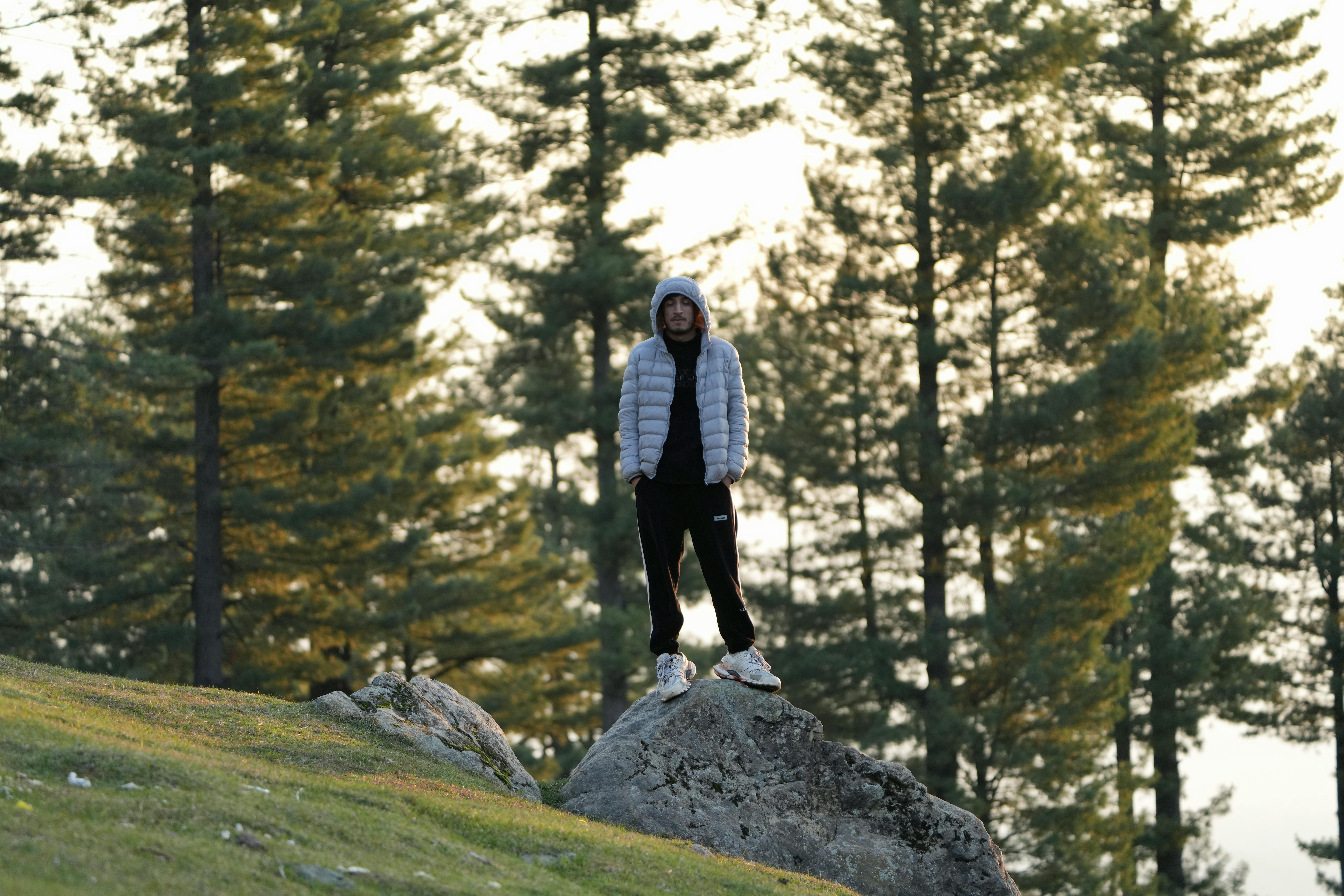 Man in warm jacket standing on a rock in forest, embracing nature's tranquility.