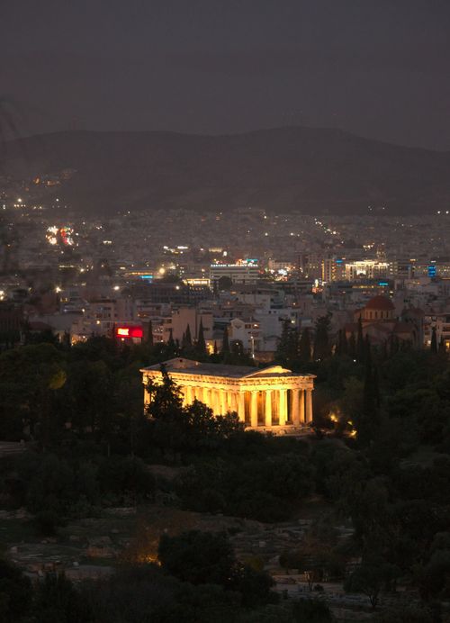 Free The Temple of Hephaestus glowing at night in Athens, Greece, amidst urban cityscape and hills. Stock Photo