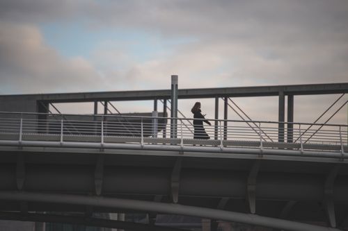 Free A woman silhouetted against the sky walks across a steel bridge in an urban setting. Stock Photo