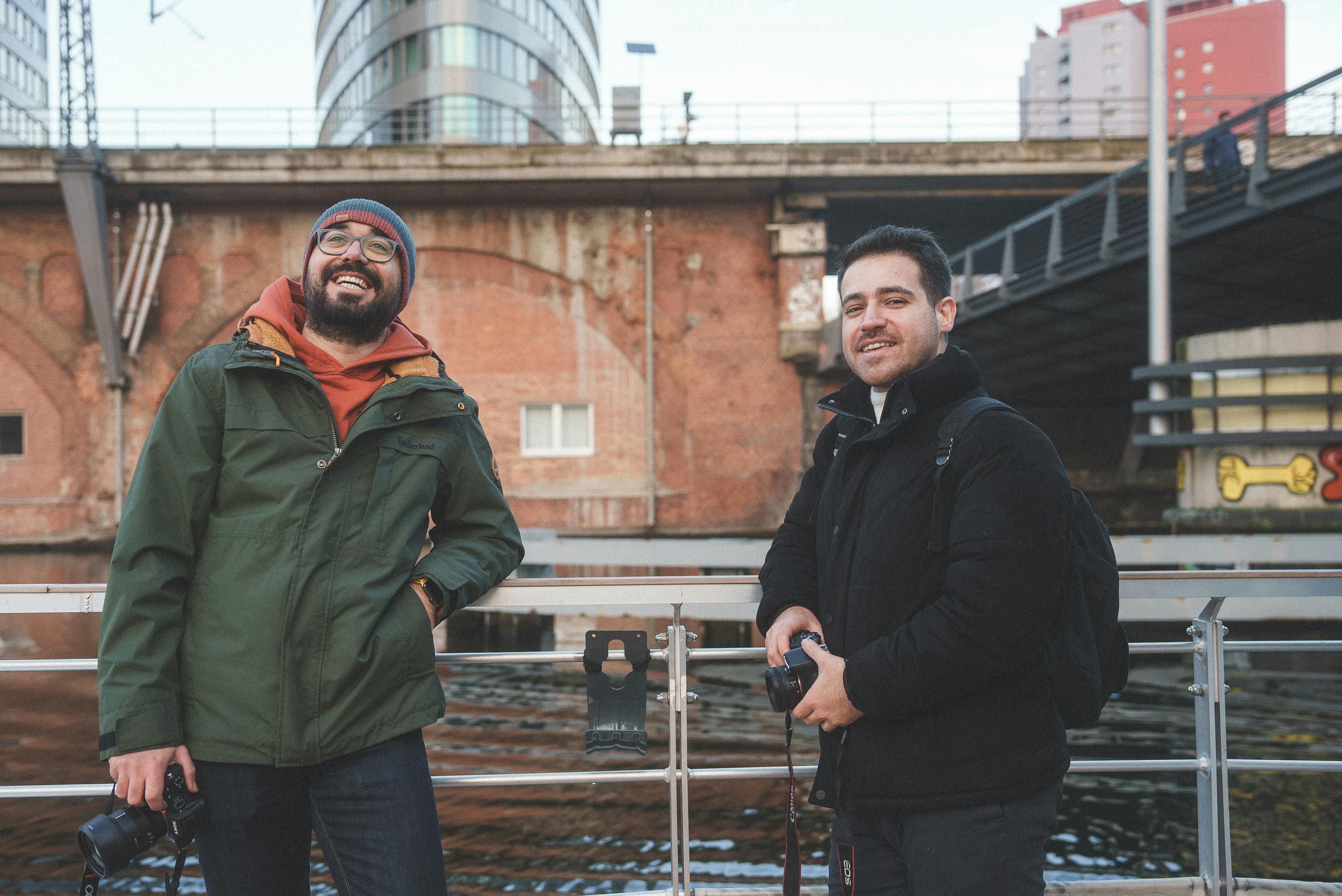 Two friends with cameras enjoying photography near a river in an urban environment.