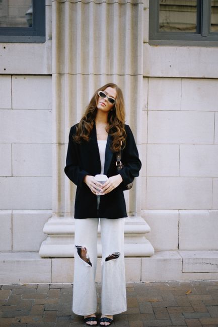 Fashionable woman in street style posing with coffee outside a building.
