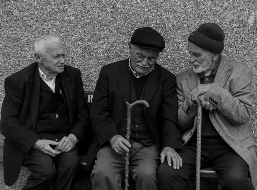 Tres ancianos con bastones disfrutan de una charla espontánea al aire libre.