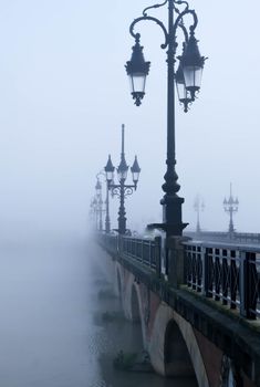Atmospheric view of lamp-lined Pontpierre Bridge enveloped in morning fog, Grand Est, France.