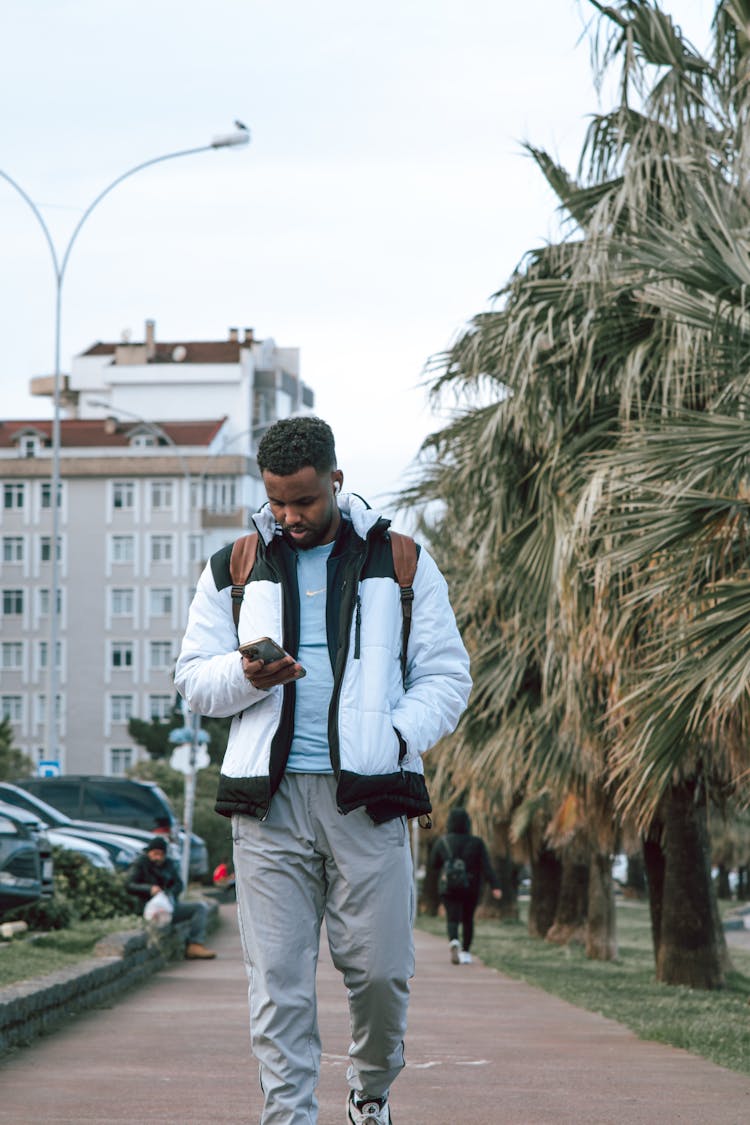 Man In Jacket Walking On Pavement With Phone In Hand