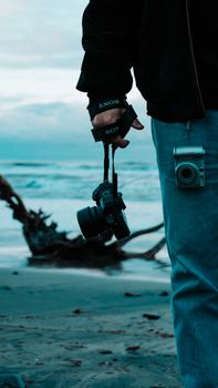 Close-up of a man holding a camera on a beach with the sea in the background.