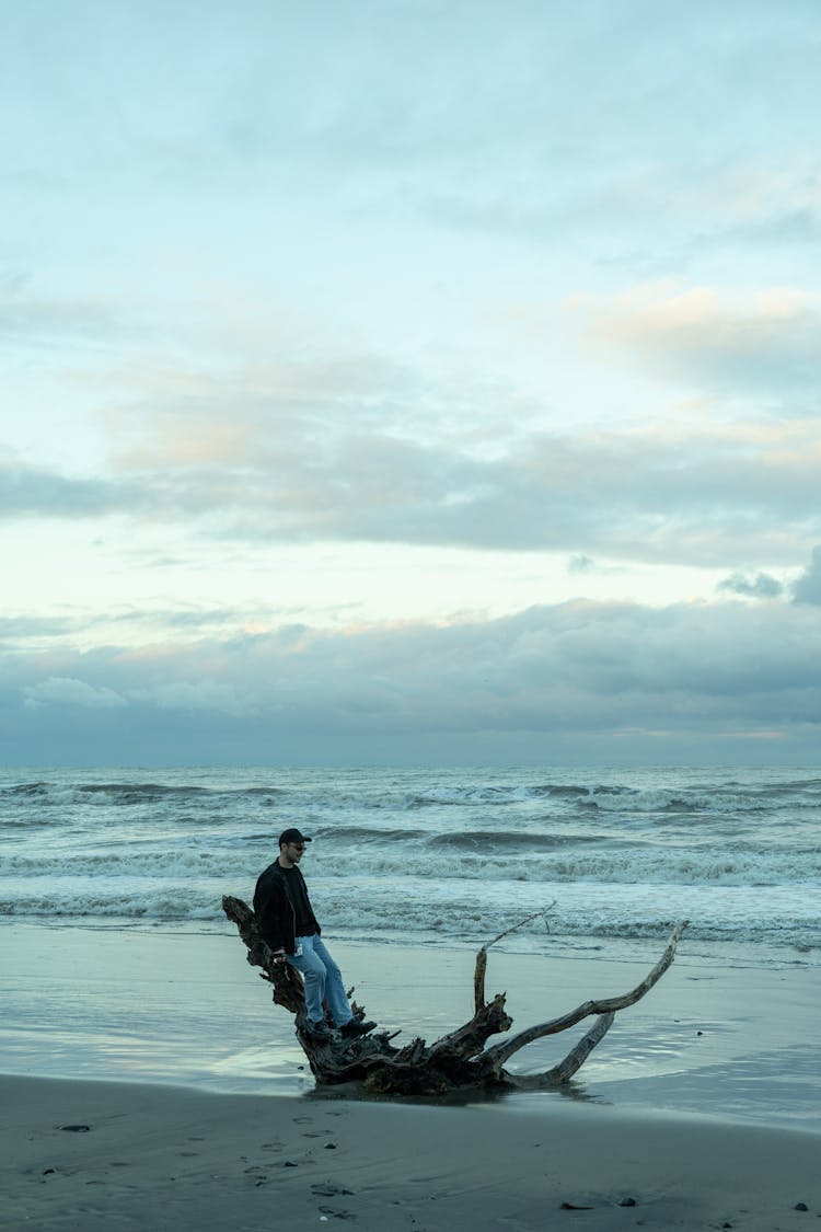 Man Sitting On The Driftwood On An Empty Beach 