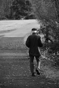 Elderly man walking alone on a peaceful forest path in black and white.