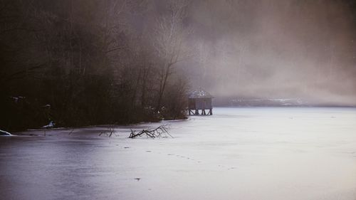Free A serene winter scene with a foggy lake and hut, embodying peaceful outdoor beauty. Stock Photo