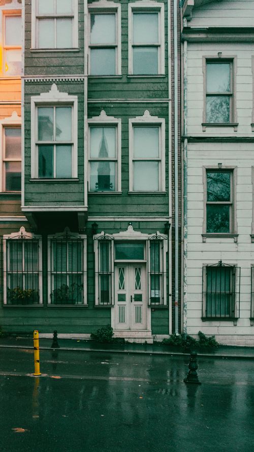 Free Charming urban townhouses on a rainy street showcasing wet pavement and classic architecture. Stock Photo