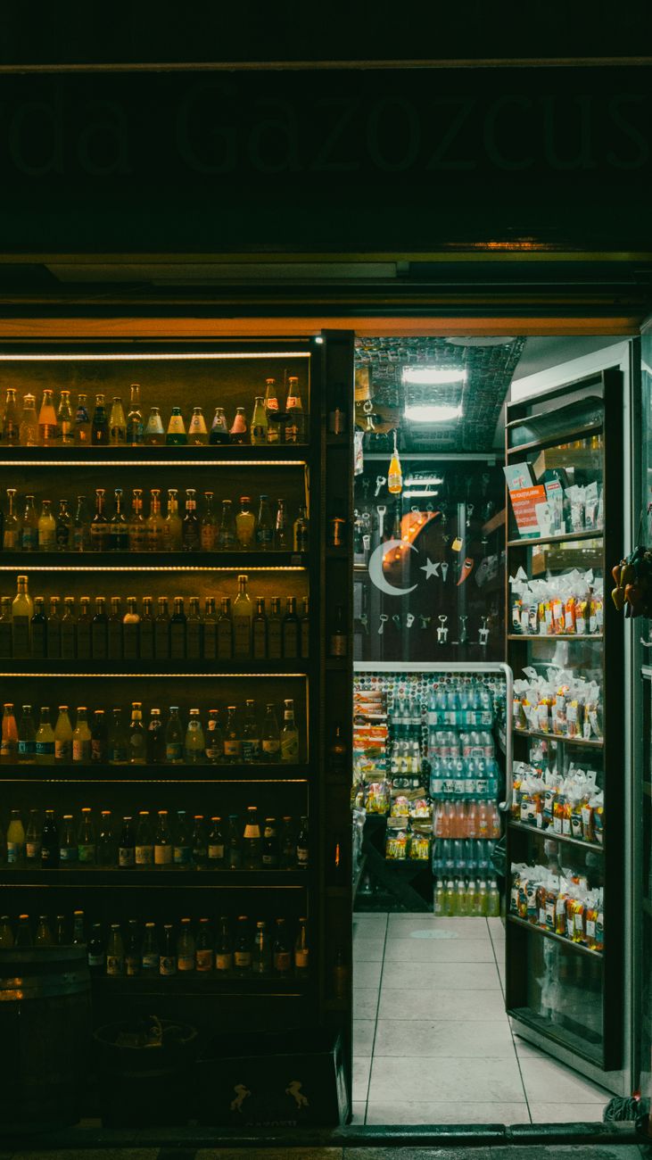 Warmly lit entrance of a small store with shelves stocked full at night.