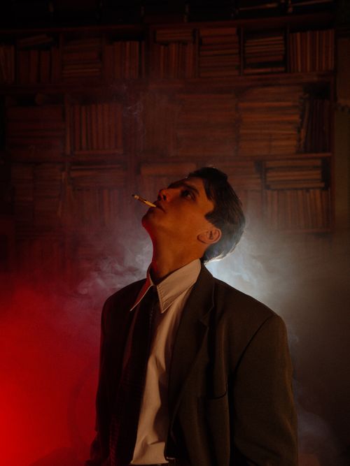 Free Moody portrait of a man in a suit with cigarette smoke, set against a dark, atmospheric background. Stock Photo