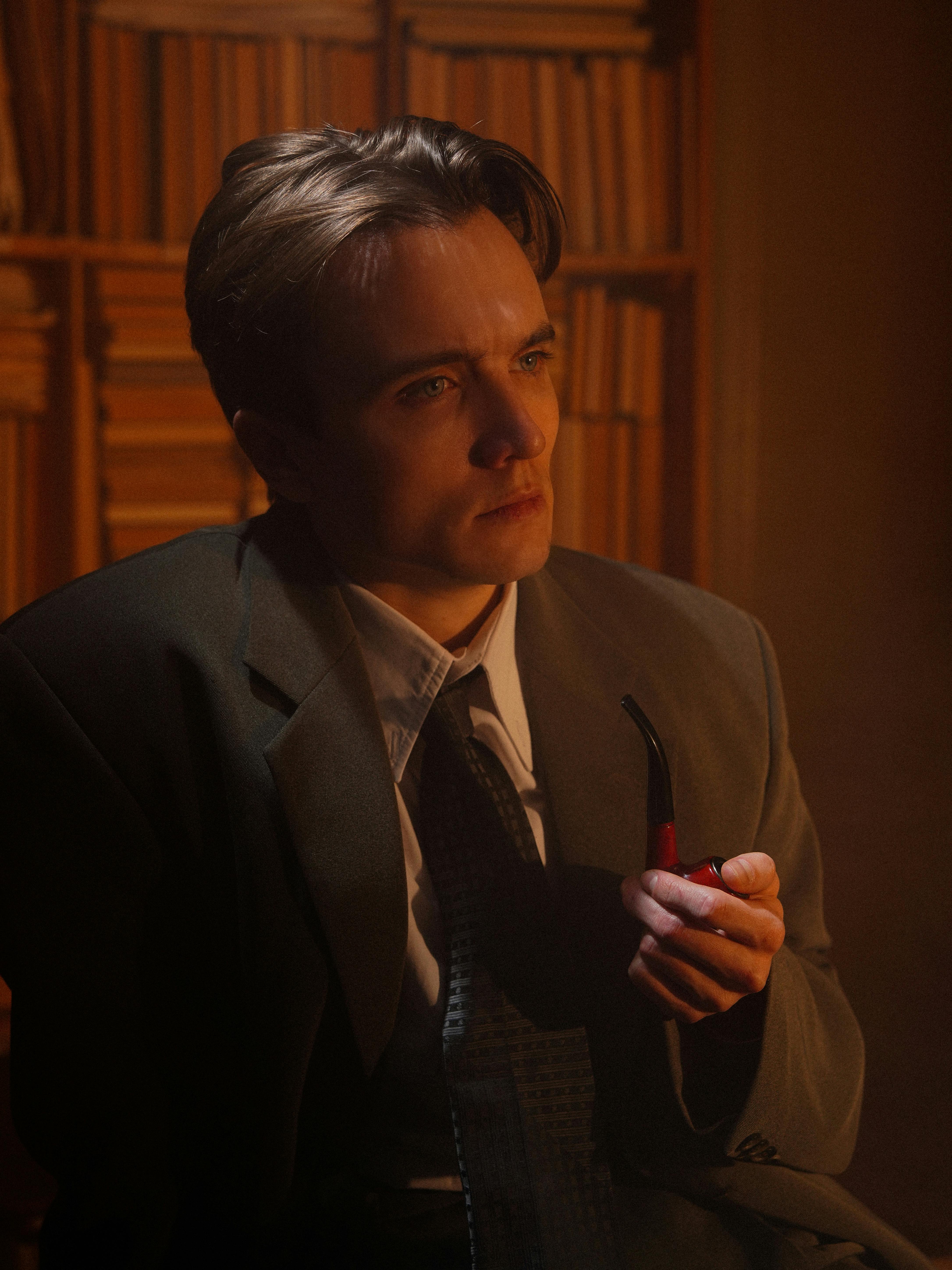 Elegant portrait of a man in a vintage suit holding a pipe, with a dramatic light setting.
