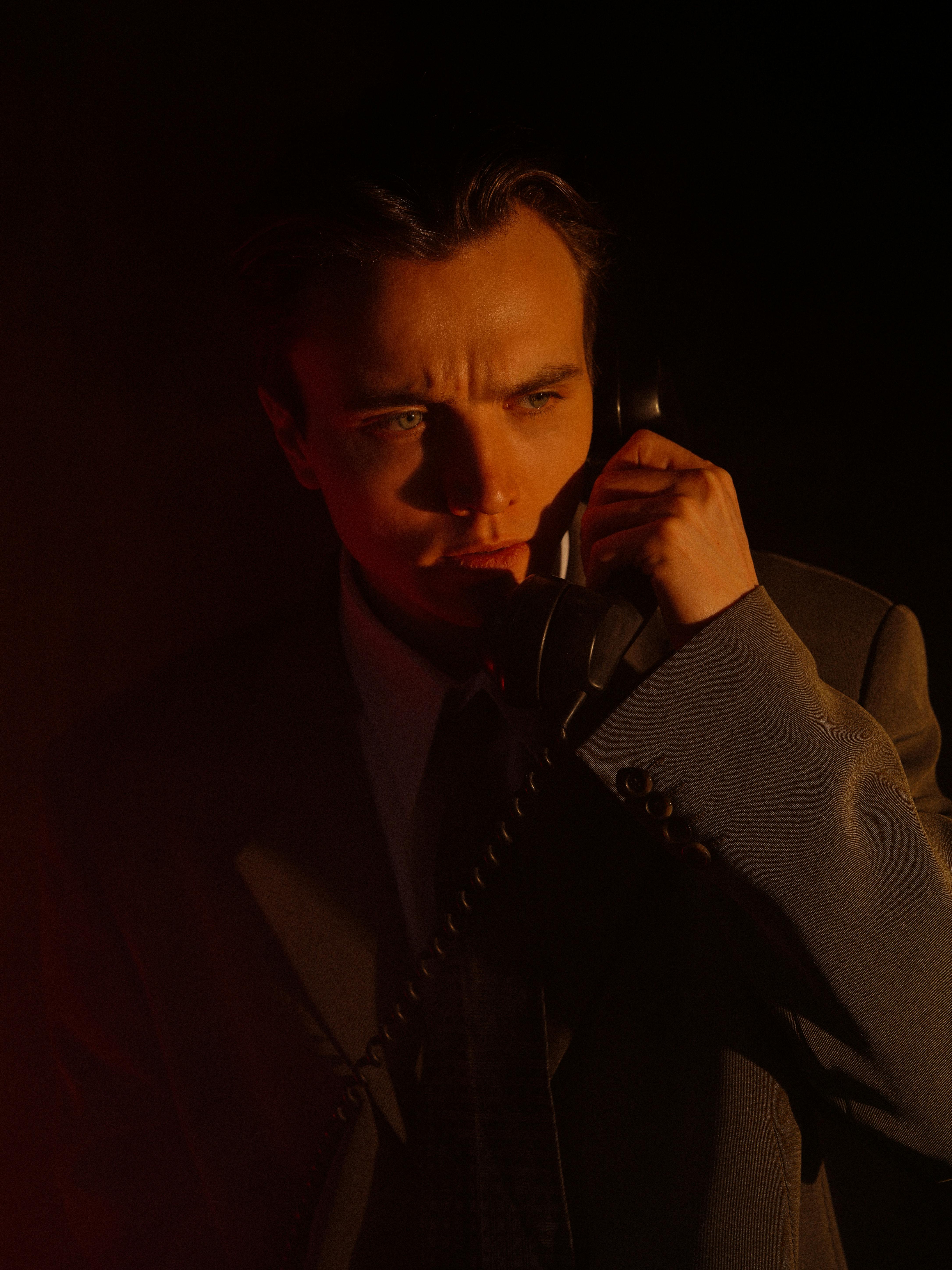 A man in a coat uses a classic phone in dramatic lighting.