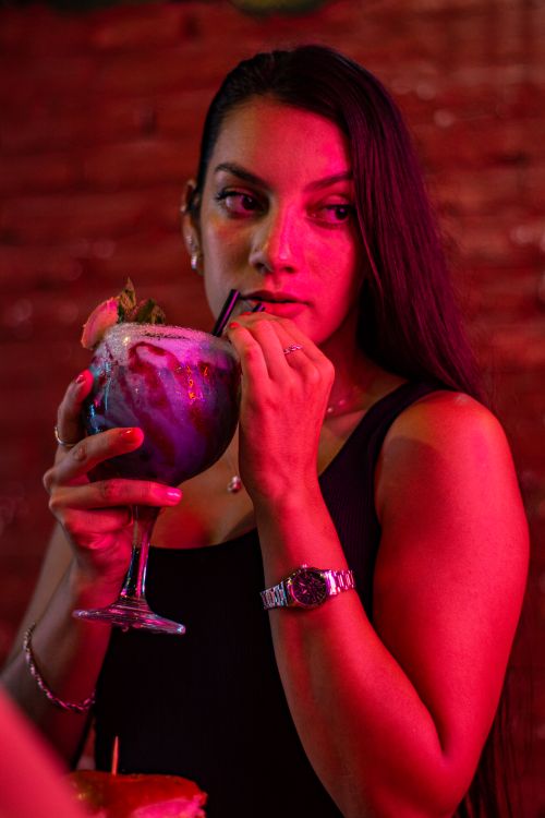 Free A woman enjoying a colorful drink in a lively bar with dramatic lighting. Stock Photo