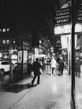 Moody black and white street photo showing pedestrians on a rainy night in the city.