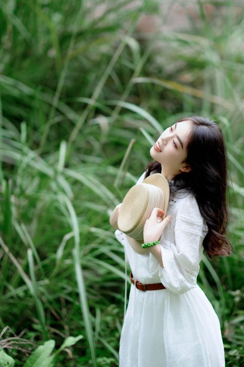 Free An adult woman enjoying a sunny day in the park, wearing a white dress and holding a straw hat. Stock Photo