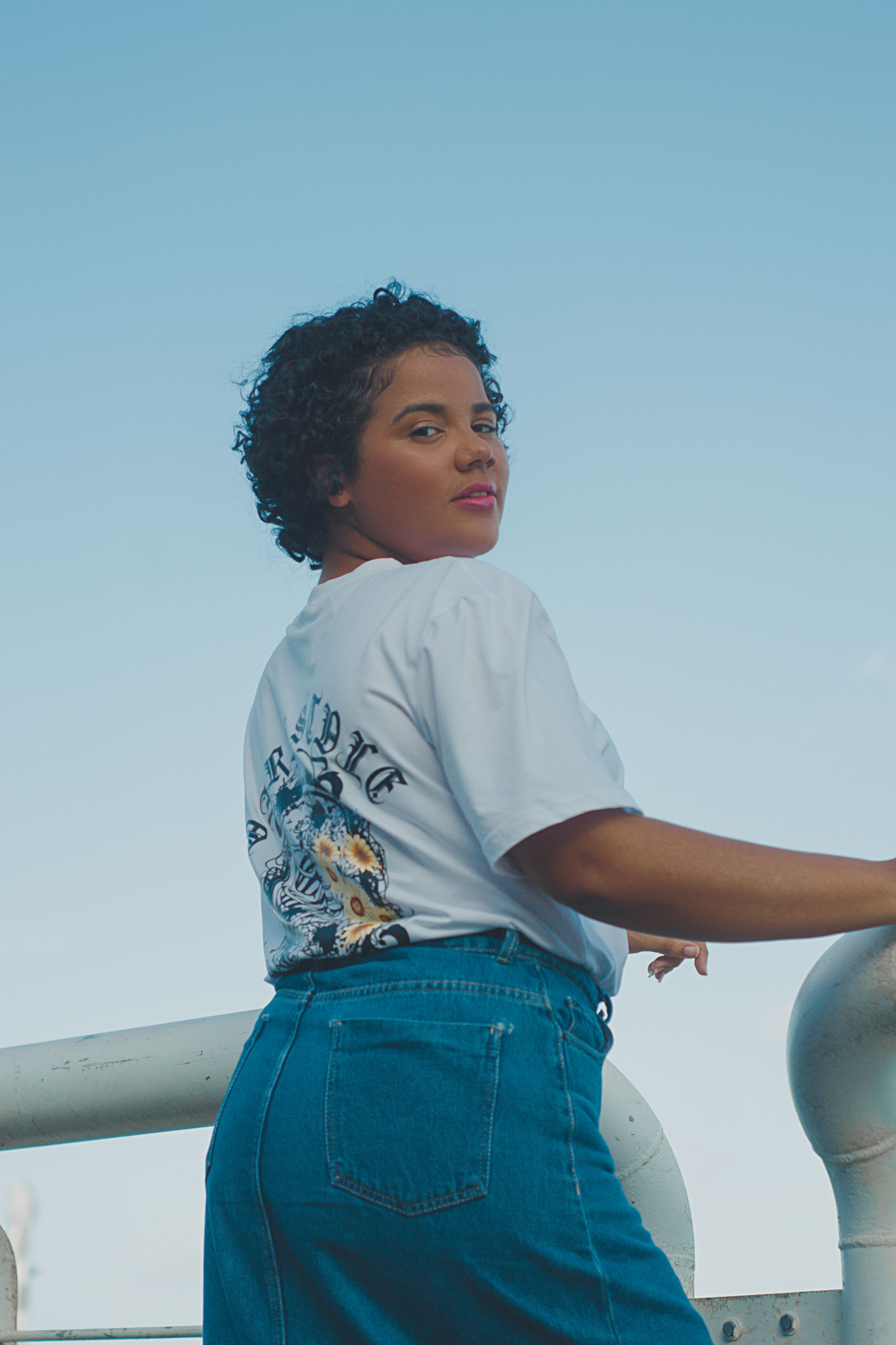 Confident woman with curly hair posing near the sea in PE, Brazil, in casual attire.