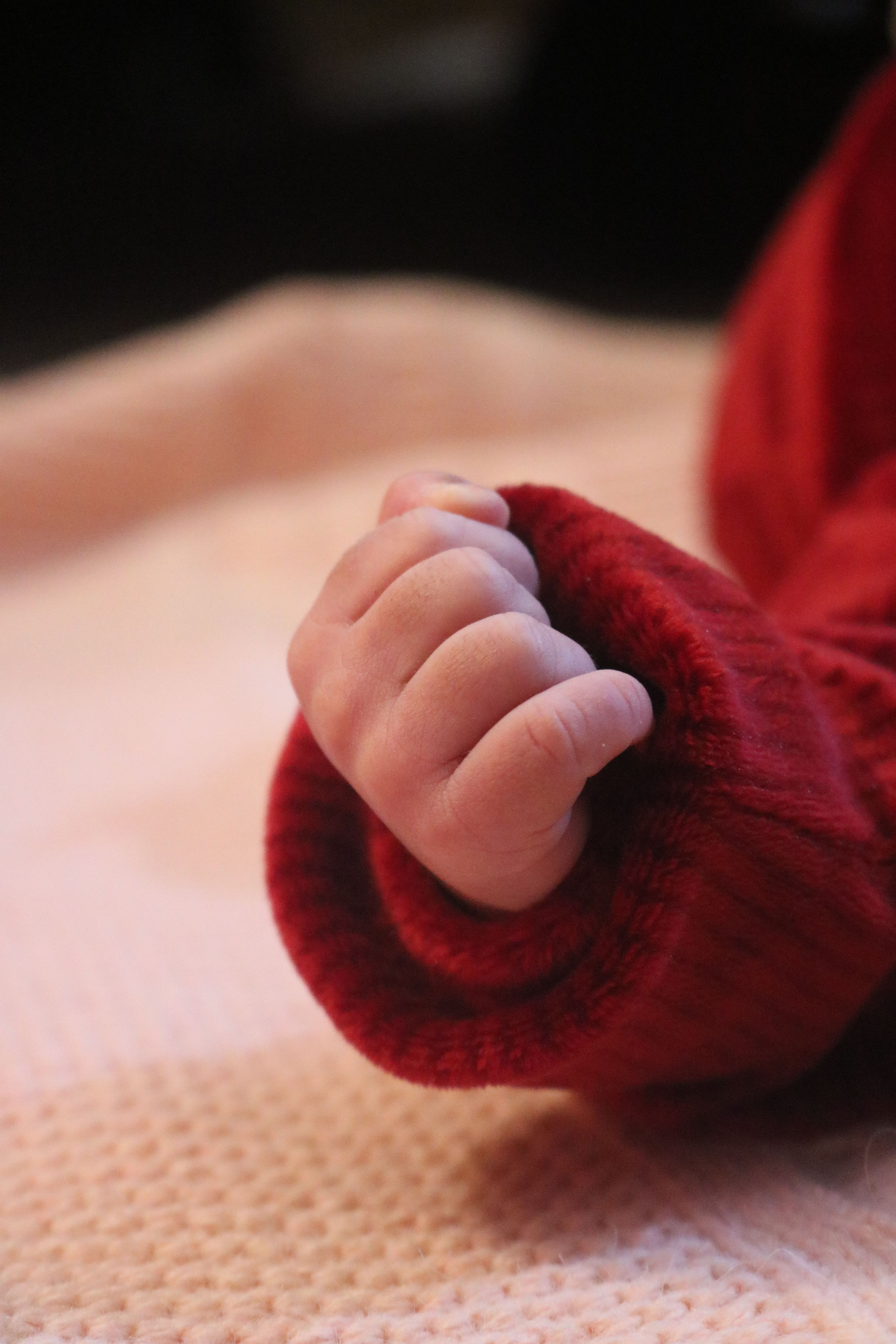 A close-up of a baby's hand in a red sweater on a soft pink blanket, showcasing warmth.