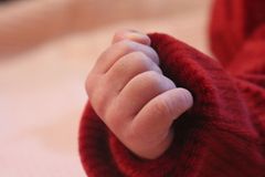 A close-up of a baby's hand in a red sweater on a soft pink blanket, showcasing warmth.