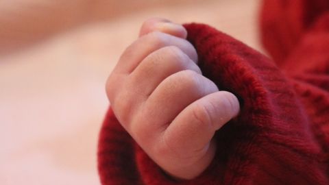 A close-up of a baby's hand in a red sweater on a soft pink blanket, showcasing warmth.