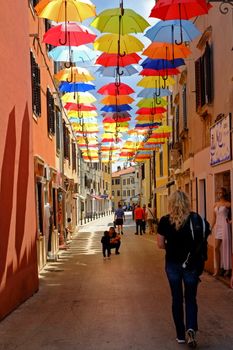 Vibrant umbrellas create a colorful canopy in a busy Novigrad street.
