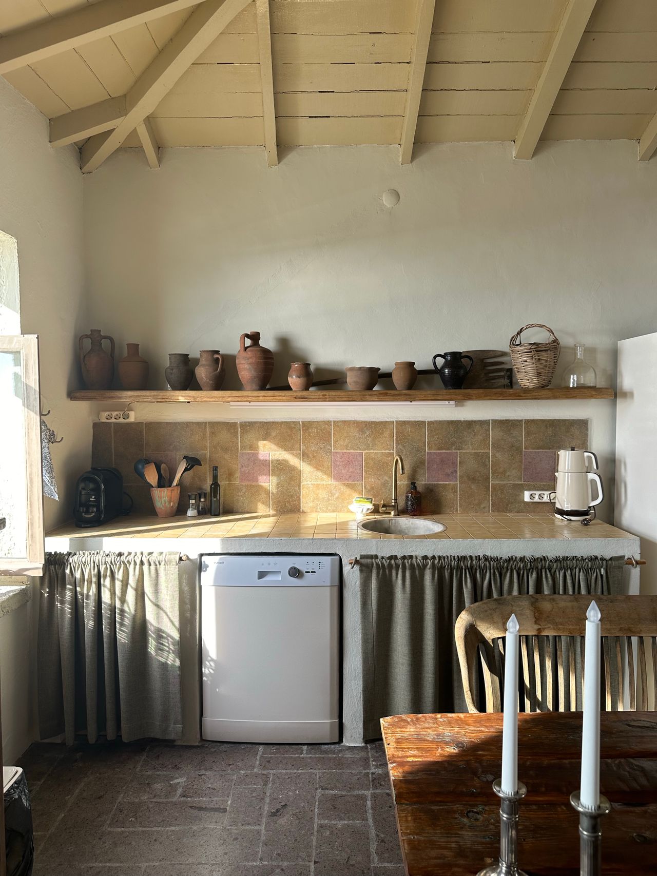 Long wooden shelf lined with clay crocks, pottery jugs and a woven basket above a country kitchen counter