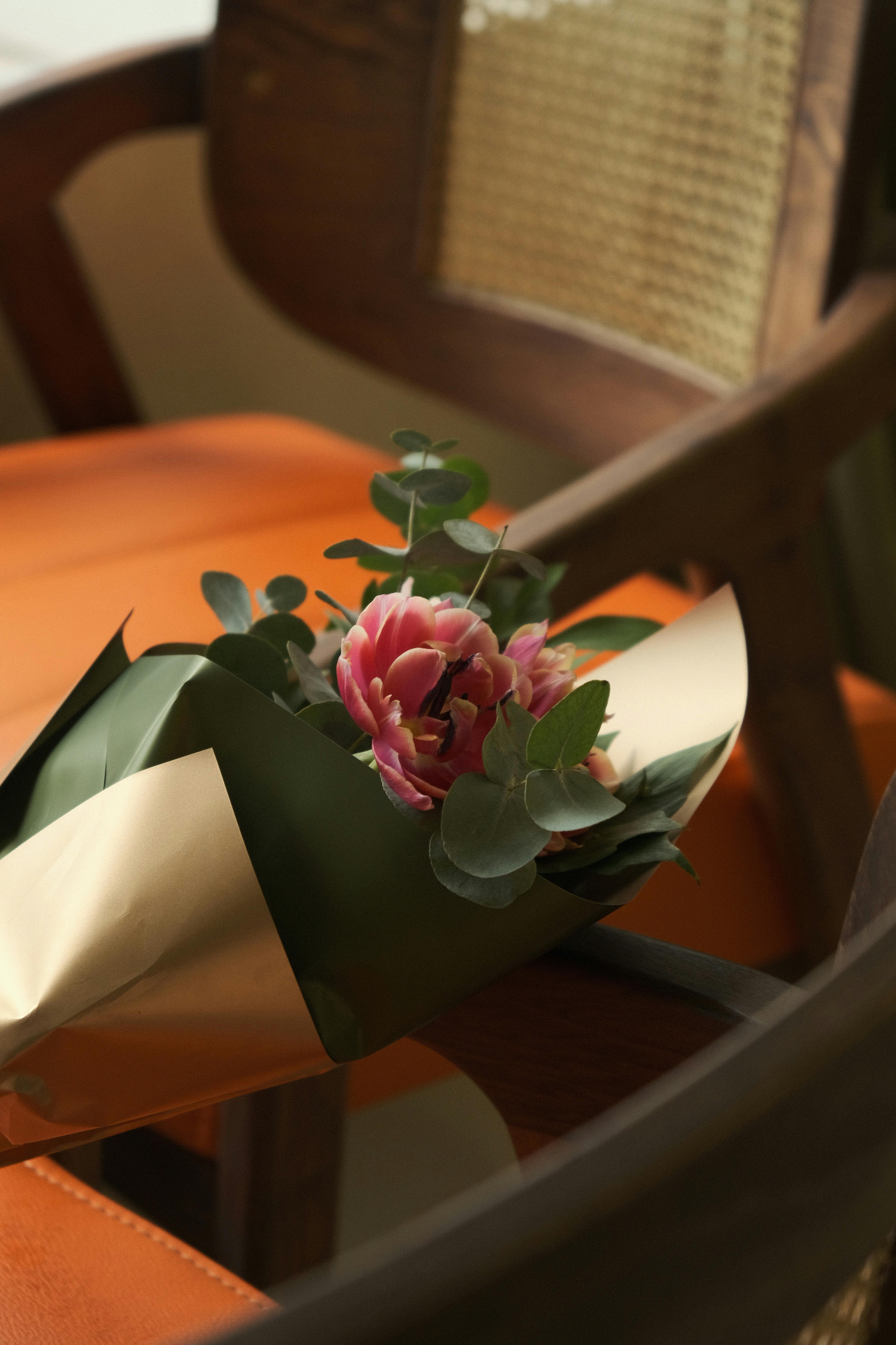 Close-up of a pink flower bouquet resting on a vintage wooden chair with orange upholstery.