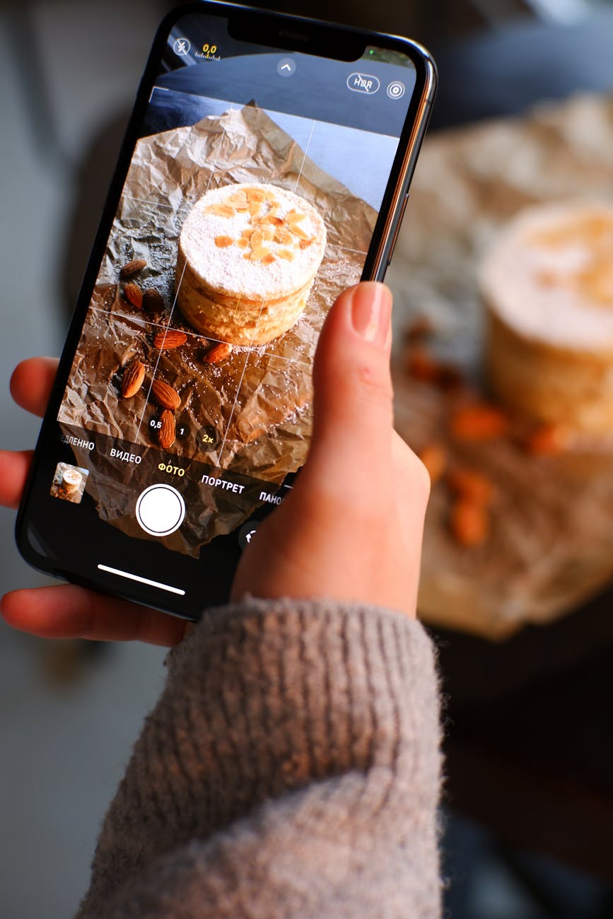 Close-up of a person photographing a cake with a smartphone, focusing on details.