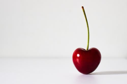 Vibrant single heart shaped cherry with stem isolated on white background. Right alignment, space for text. Health, nutrition and healthy eating concept