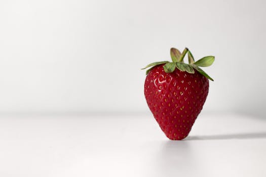 A single ripe strawberry with vibrant red color on a minimalist white backdrop, highlighting its freshness and natural beauty.