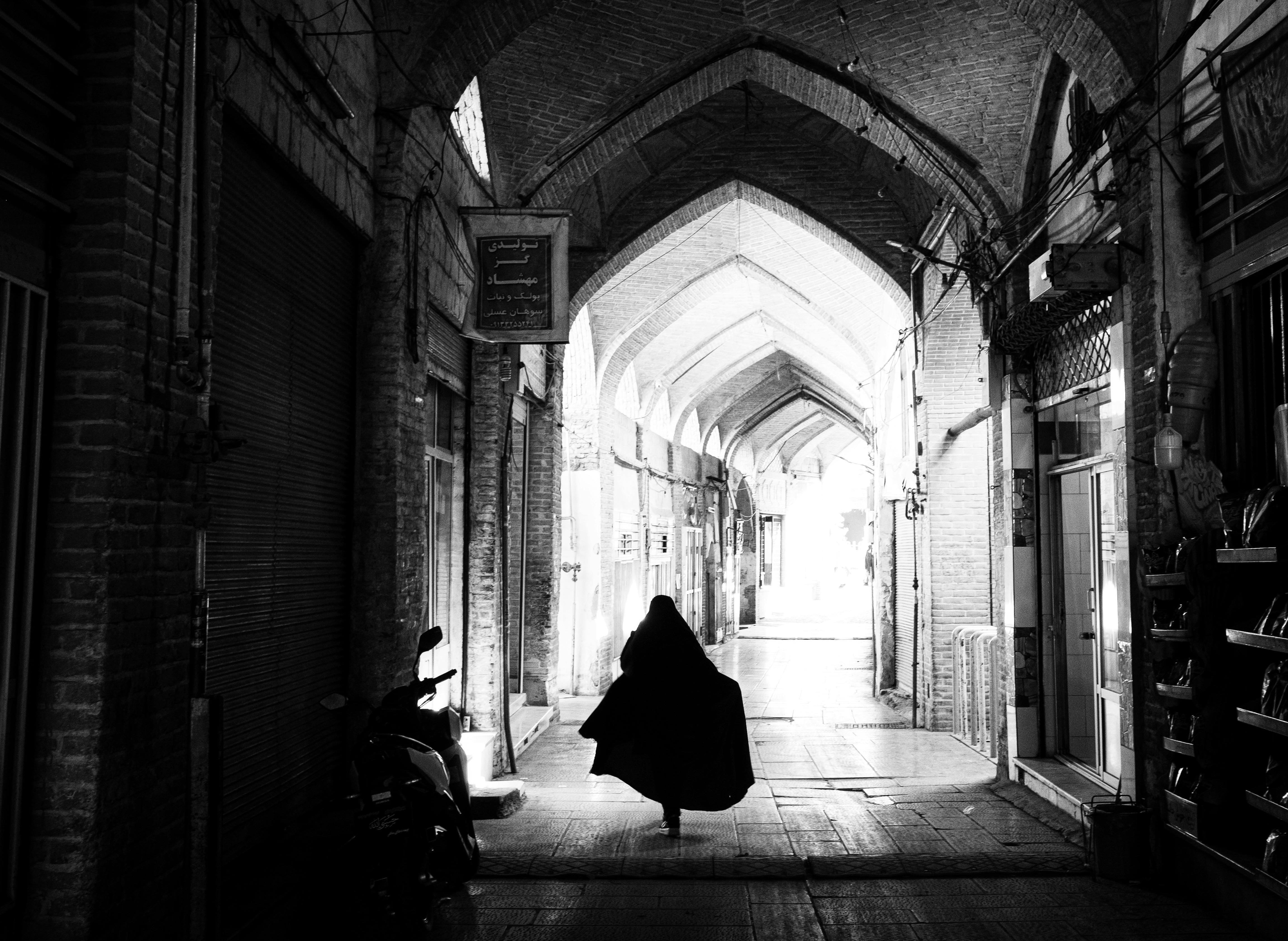 A striking black and white silhouette of a woman walking through the historic bazaar corridor in Isfahan, Iran.